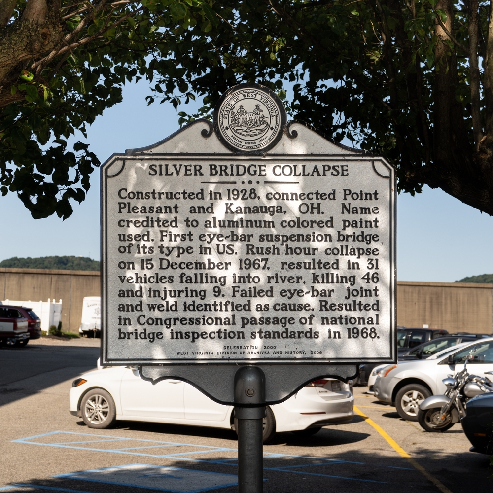Historical marker in Point Pleasant, West Virginia, describing the 1967 Silver Bridge collapse, with a backdrop of parked vehicles.