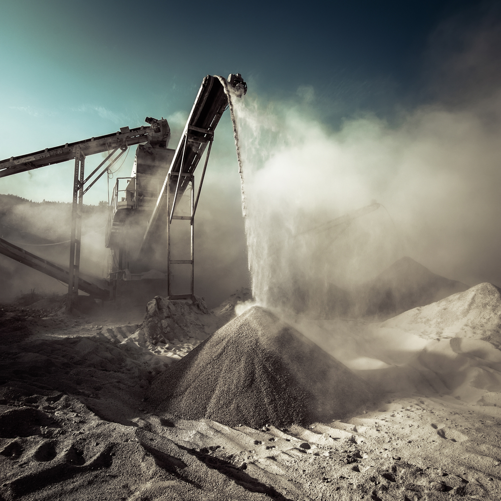 Industrial machinery processing concrete with rising dust.